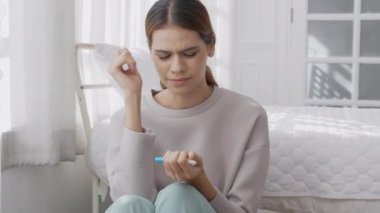 Beautiful young caucasian woman expression with depressed and unexpected after looking pregnancy test result in the bedroom at home, motherhood and mistake, one person, lifestyles concept.