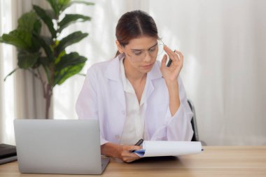Genç kadın doktor dizüstü bilgisayar kullanıyor ve klinikte teşhis için hasta hakkında belgeler arıyor, doktor kadın panoda çalışıyor ve belgeleri okuyor, bir kişi, tıbbi konsept.