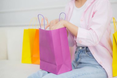 Closeup hands of woman sitting on sofa open paper bag while online shopping with credit card at home, girl purchase and discount of consumer with excited, shopaholic and lifestyles concept.