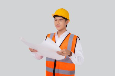Portrait young asian man is engineer wearing helmet holding and looking blueprint with confident isolated on white background, handsome male is architect or contractor, worker or labor concept.