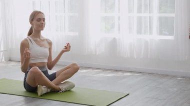 Yoga yapan ve rahatlamak için meditasyon yapan genç bir kadın. Evde paspas üzerinde hayatı dengeleyen bir kadın. Rahatlama, sağlık ve spor konsepti için kadın oturma ve egzersiz yogası..