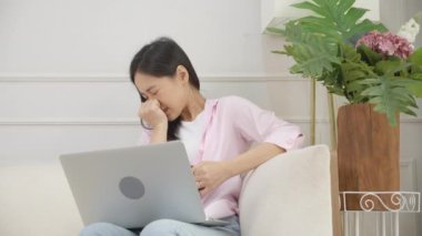 Genç Asyalı iş kadını dizüstü bilgisayarında korku filmi seyrediyor oturma odasındaki koltukta korkmuş ve korkmuş bir şekilde. Not defteri kullanan bir kız rahat ve rahat bir şekilde koltukta oturuyor..