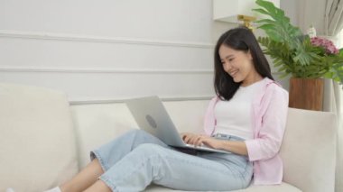 Young asian business woman work from home with laptop computer online to internet on sofa in living room, freelance girl using notebook sitting on couch with comfort and relax, lifestyles concept.