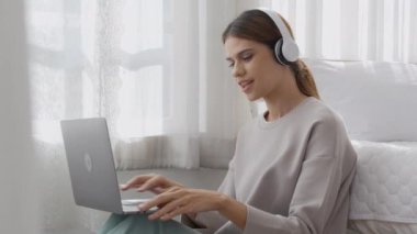 Happy young woman wearing headphones listening music while using laptop computer and singing with fun and enjoy in the living room, happiness female with entertainment, lifestyles concept.