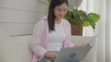 Young asian business woman working on laptop computer and looking graph and chart of report for profit on paper at home, businesswoman looking investment and income, data of infographic statistics.