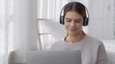 Happy young woman wearing headphones listening music while using laptop computer and singing with fun and enjoy in the living room, happiness female with entertainment, lifestyles concept.