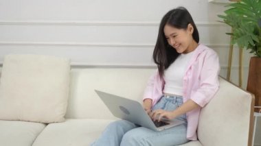Young asian business woman work from home with laptop computer online to internet on sofa in living room, freelance girl using notebook sitting on couch with comfort and relax, lifestyles concept.