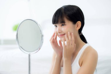 Mutlu gülümseyen ve yanak aynasına dokunan güzel Asyalı bir kadının güzel yüzü. Cilt bakımı, cilt bakımı, cilt bakımı ve sağlıklı bir konsepti olan güzel bir yüz makyajı..