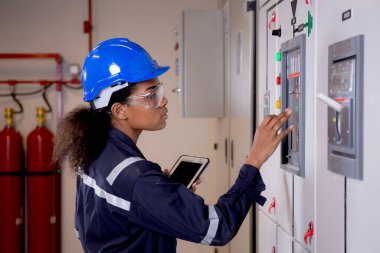 Electrical young asian woman engineer examining maintenance cabinet system electric and using tablet in control room at industrial factory, technician or electrician inspection power distribution.