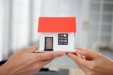 Genç emlakçı emlakçının yakın elleri müşteriye ev modeli verirken anlaşma ve sözleşme başarısı ve ev idaresi, yatırım ve ipotek, iş konsepti.