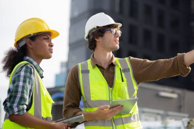 Young man and woman is architect planning and inspector project and looking digital tablet at construction site, engineer male and female working and examining for development real estate.