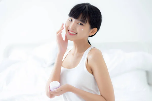 Beautiful young asian woman holding cartridge applying cream or lotion with moisturizer to skin on face, beauty asia girl applying skincare touch facial with cosmetic makeup, skin care concept.