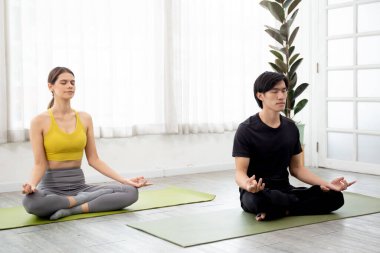 Yoga ve meditasyon yapan genç erkek ve kadın evdeki paspasın üzerinde hayatı dengelemek için meditasyon yapıyorlar. Kadın ve erkek oturma ve egzersiz yoga, sağlık ve spor konsepti..