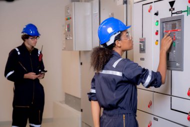 Elektrikli genç Asyalı kadın ve erkek mühendis, endüstriyel fabrika, teknisyen ya da elektrikçi denetleme güç dağıtımının kontrol odasındaki kabine sistemini inceliyor..