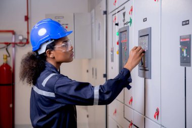 Electrical young asian woman engineer examining maintenance cabinet system electric and using tablet in control room at industrial factory, technician or electrician inspection power distribution.