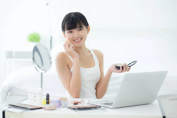 若いアジアの女性の美しさとともに化粧を学びますパウダーパフ頬にラップトップコンピュータを見ますチュートリアルコースオンラインで 女性の教育とストリーミングメディア上の化粧品で構成され説明 — ストック写真