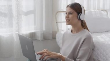 Happy young woman wearing headphones listening music while using laptop computer and singing with fun and enjoy in the living room, happiness female with entertainment, lifestyles concept.