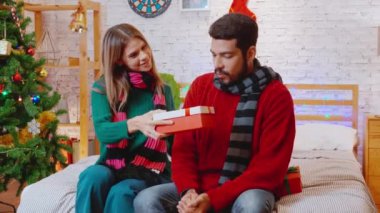 Genç bir kadın sürpriz erkek arkadaşına Noel 'i evde kutlarken hediyeler veriyor, kız arkadaşı da heyecanlı, olaylı ve şenlikli hediye kutlaması yapıyor, xmas ve yeni yıl ya da tatil konsepti..