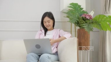 Happiness young asian woman sitting on sofa and working on laptop computer while successful and excitement at home, freelance female using notebook and achievement, business and lifestyles concept.