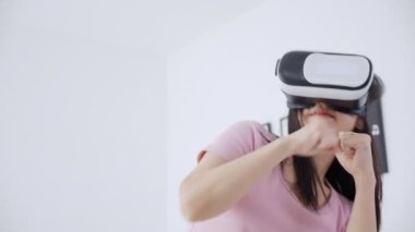 VR kulaklık takan genç Asyalı bir kadın evdeki yatak odasındaki yatakta heyecanla oyun oynuyor. Sanal gerçeklik ya da metaz yeniliklerini kullanarak 3 boyutlu, yaşam tarzları ve teknoloji kavramını kullanıyor..