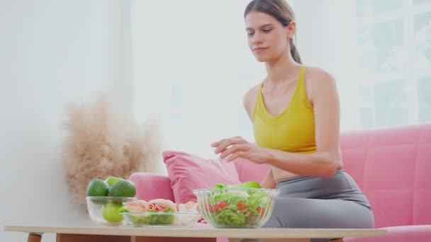 漂亮的年轻高加索女人坐在沙发上 手里拿着碗三明治和沙拉蔬菜 选择在家吃饭 食物和营养促进健康 饮食促进减肥 生活方式观念 — 图库视频影像