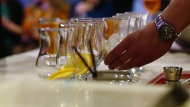 Profesyonel barmen bardaklara buz ve portakal koyar.