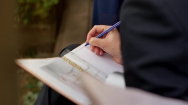 Takım elbiseli genç bir kız, bir yaz günü bir bankta otururken not defterine not alır..