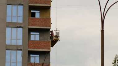 Çok katlı bir binanın inşaatı sırasında, inşaatçılar açık havada, inşaat alanında asansörde çalışırlar.
