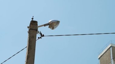 Sokak lambası, çok katlı bir bina ve mavi gökyüzünün arka planında.