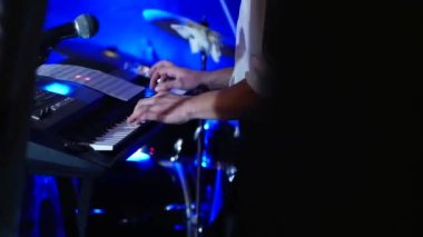 Sentezleyici çalan bir klavyecinin eline yakın plan. Genç bir adamın parmakları davulun arka planına karşı müzik aletinin tuşlarına basar..