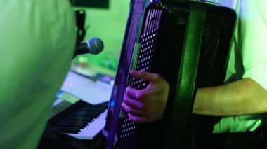 Müzikal bir performans sırasında akordiyonu mikrofona çalan bir müzisyenin yakın çekimi. Genç bir adamın parmakları bir müzik aletinin tuşlarına basıyor.