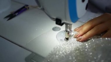 Tekstil endüstrisindeki bir terzi, beyaz bir kumaştan dikiş makinesine kadın elbisesi diker. Manikür kumaşlı kadın elleri dikiş makinesinde endüstriyel dikiş makinesine tıkıştırılıyor.