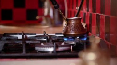 Kırmızı ve siyah bir mutfakta bakır bir Türk Türkünün gaz ocağında kahve yapmak..