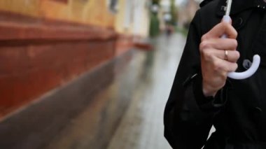 Sonbahar yağmuru sırasında, bir kadın elinde beyaz bir şemsiye ile caddede yürür. Parmağında yüzük ve şemsiye sapı olan bir elin yakın çekim videosu..