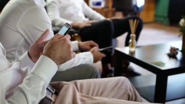 Bir grup genç adam kanepede oturup sohbet ediyorlar. Tişörtlü bir grup adamla sohbet etmek. Bir arkadaş şirketinin arka planında elinde akıllı telefon tutan genç bir adamın yakın plan fotoğrafı.