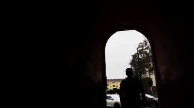  Arka planda, bir adam tünelden geçerek şehrin arka planına doğru yürür. Bir adam konut binasının oval kemerine giriyor..