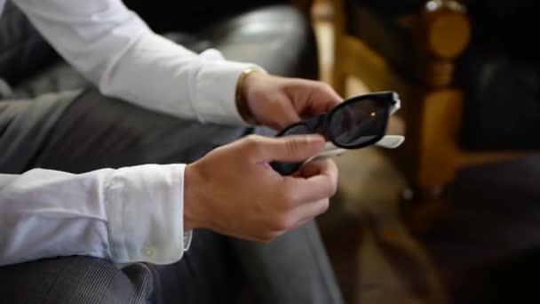 シャツとズボンを着た若い男が手にサングラスを持っている クローズアップビデオ撮影黒眼鏡 — ストック動画