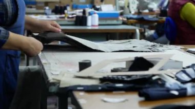 Bir kadın giyim fabrikası işçisi kesme ve dikmeye hazırlanırken bir kumaş parçasını çalışma masasının üzerine doğrultuyor. Tekstil kesiciler iş başında.