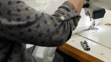 Tekstil endüstrisindeki bir terzi kadınları dikiş makinesine dikiyor. Dikiş fabrikasında kumaşı endüstriyel dikiş makinesine bağlayan kadınların yakın çekim görüntüleri.