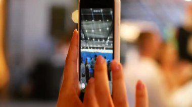 Telefonun kadın eliyle yakın plan çekimleri. Genç bir kız, bir partide dans eden genç bir adamın akıllı telefonuyla video çekiyor..