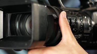 lose-up of the videographer's hand as it turns the zoom ring, turns on the ND filter, and adjusts the aperture value. The videographer focuses and adjusts the video camera in the studio before filming