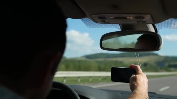 A young guy takes pictures of a mountain landscape through the windshield of a car driving on a freeway. Tourists travel the world.