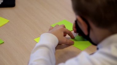 Okul dersinde bir çıkartmaya kalemle resim çizen tanınmamış küçük bir çocuğun yakın çekimi. Oğlan sınav sırasında testi bir parça kağıda yazmaya hazırlanıyor..