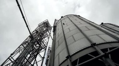 Bulutlu gökyüzüne karşı tohumları kurutmak ve depolamak için metal asansör tankları. Modern tahıl terminali. Ticari tahıl kurutma tesisi. Gökyüzü arka planında tahıl ambarları. Tarımsal hasat için çelik deposu.