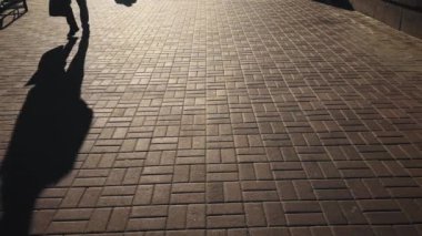 Sabahın erken saatlerinde sokakta yürüyen insanların uzun gölgeleri. Sokak alayı. Bir grup yayanın arasında bisiklet süren bir adamın gölgesi..