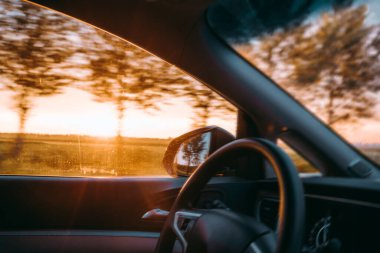 Bir araba gün batımının altında yolda gidiyor.