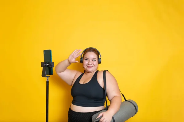 plus size model with sportswear waving to the mobile phone in online sports class to lose weight