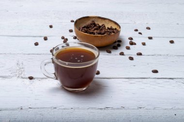 Kahve dükkanındaki tahtaların üzerinde organik kahve çekirdeğinin önünde şeffaf bir fincan kahve.