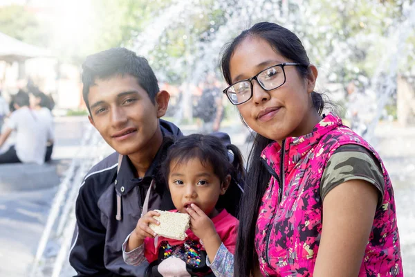 portrait of young mexican family sitting in park fountain. latin people