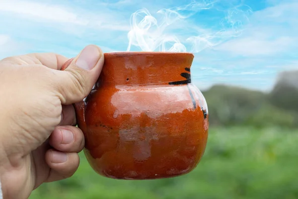 personal perspective of man holding tradonal cup of mexican coffee in field